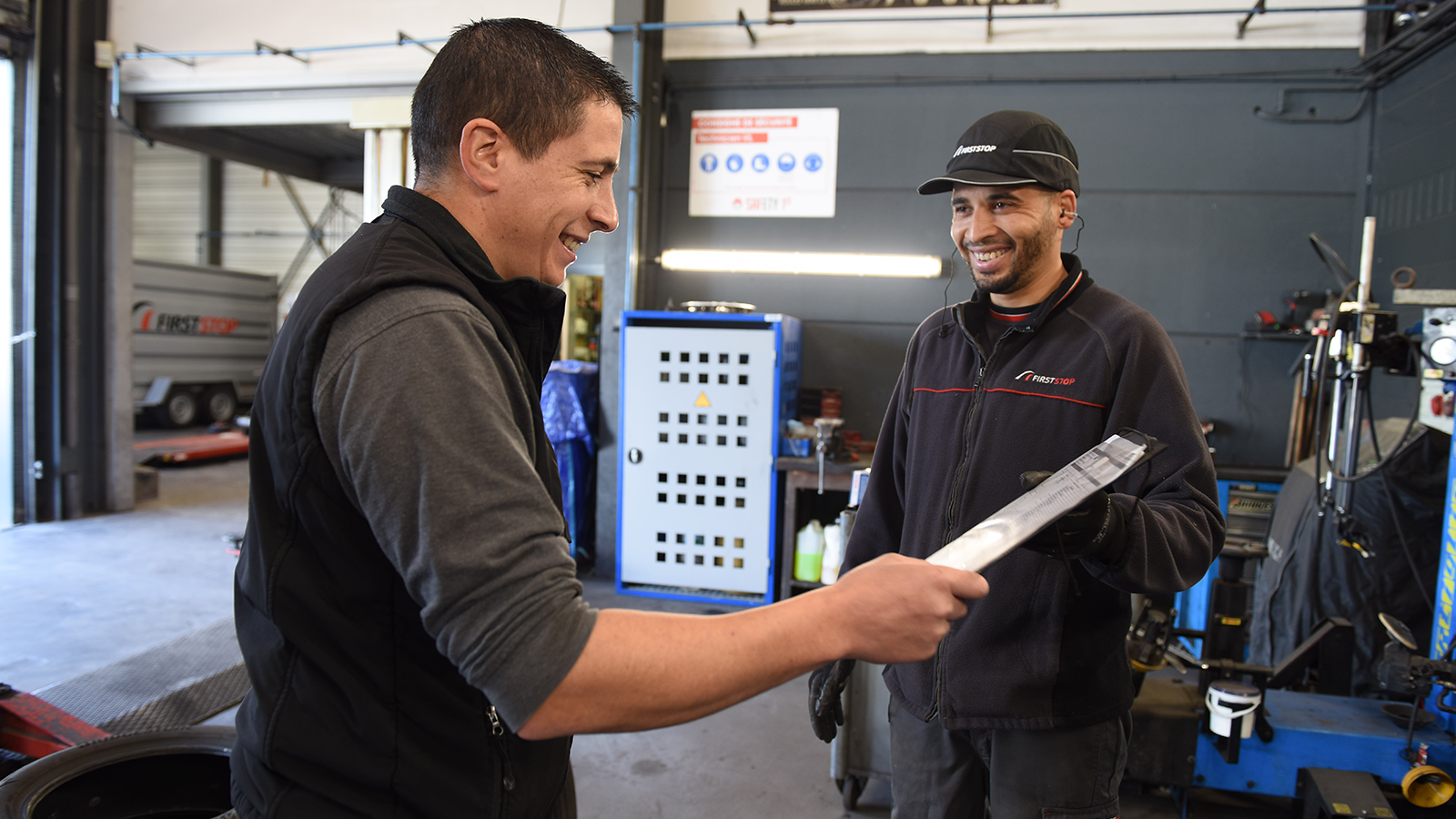 a man holding a clipboard with another man in a garage