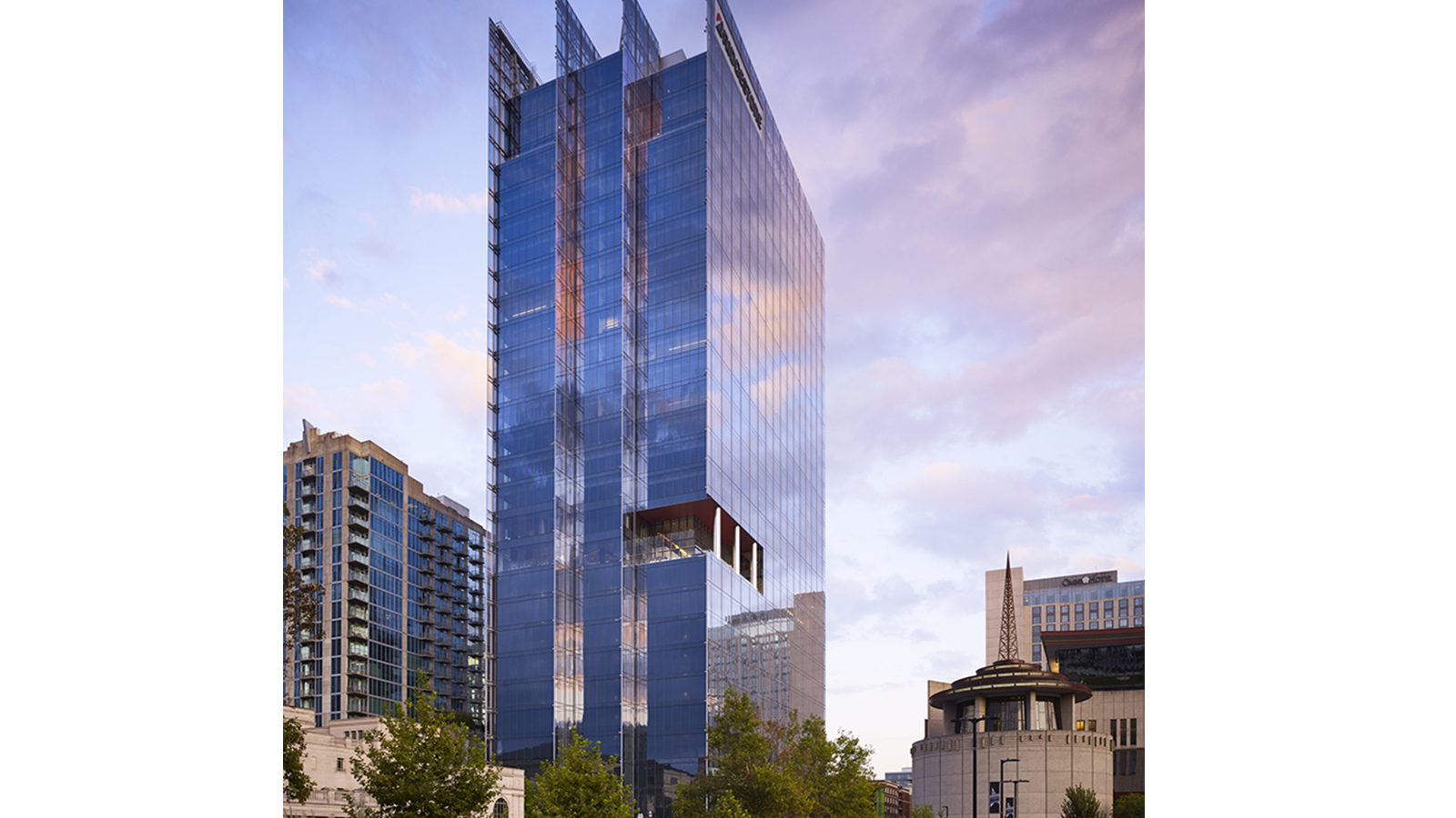 a tall glass building with trees and a blue sky