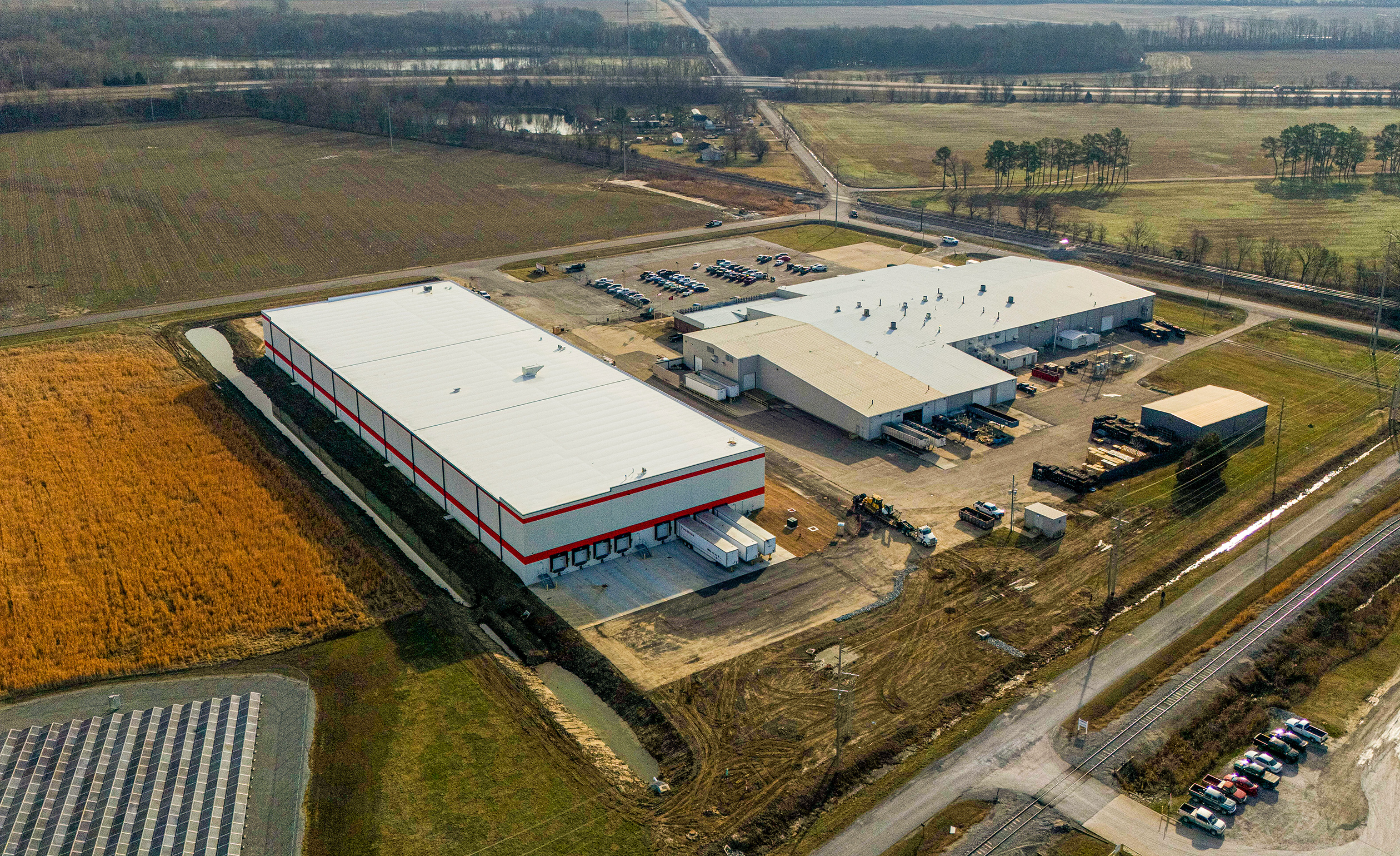 a large warehouse building with trucks parked in a field