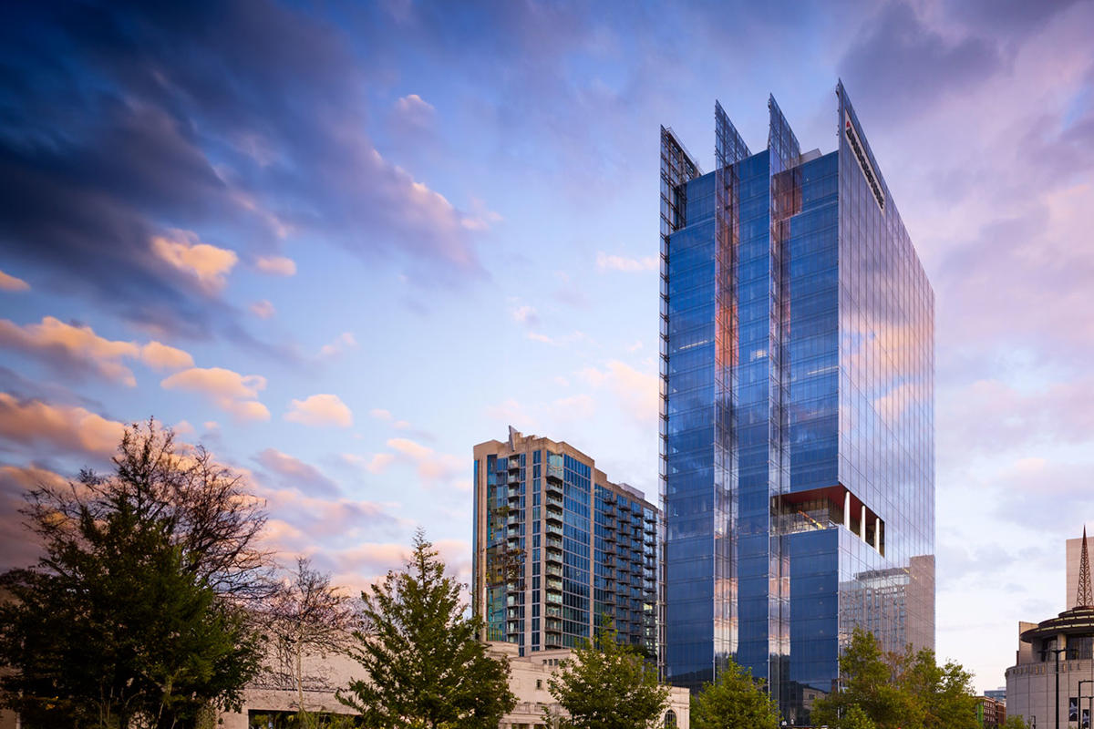 a tall glass building with trees and buildings in the background